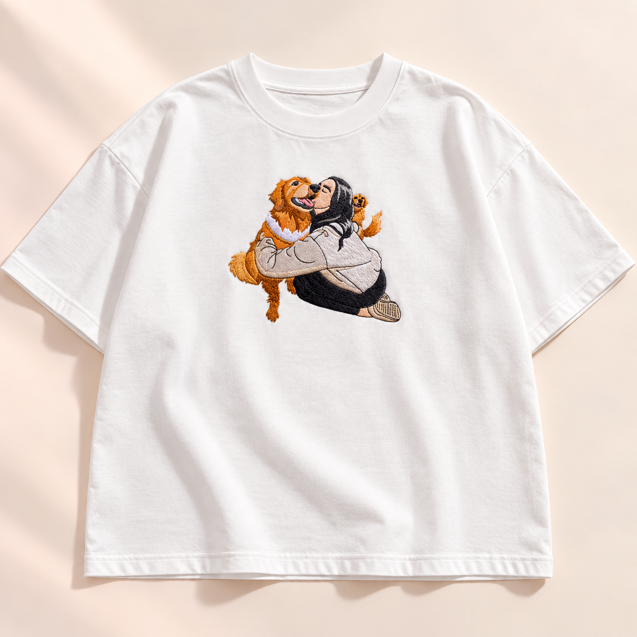 Studio flatlay of an oversized white T-shirt with a centered embroidered person-and-dog portrait