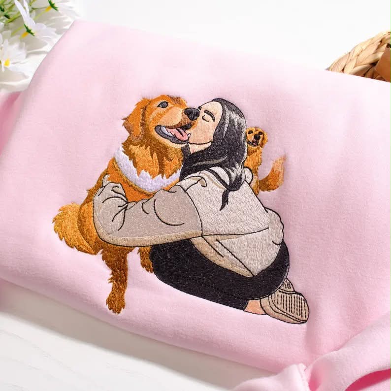 Close-up of a person hugging a golden retriever embroidered on blush pink cotton
